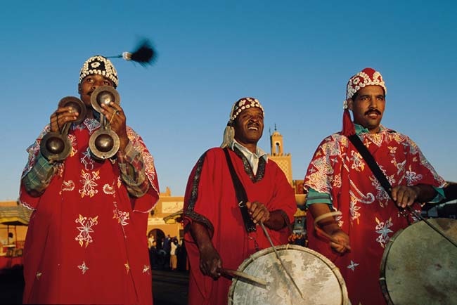 Gnaoua musicians in red embroidered robes playing qraqeb metal castanets and drums in Essaouira, Morocco