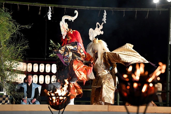 Noh actors in silk robes and wooden masks performing Takigi Noh by bonfire at Heian Shrine in Kyoto