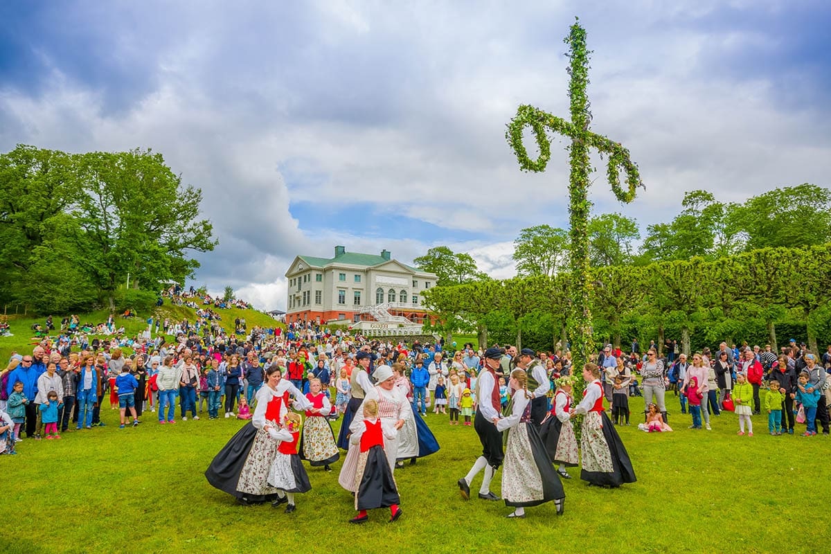 Swedish midsummer maypole decorated with birch leaves and wildflowers, surrounded by dancers in folk dress